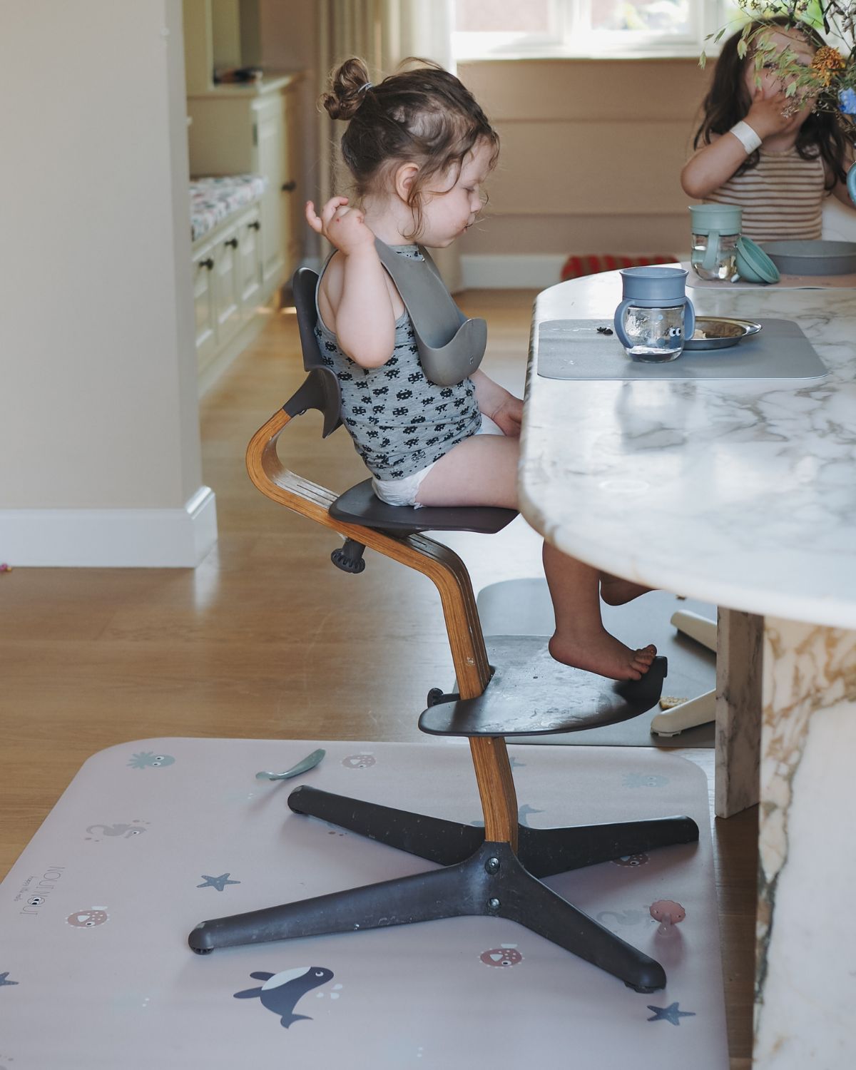 A rectangular high chair floor mat with a pattern of various ocean animals, such as whales and octopuses, on a nude background.