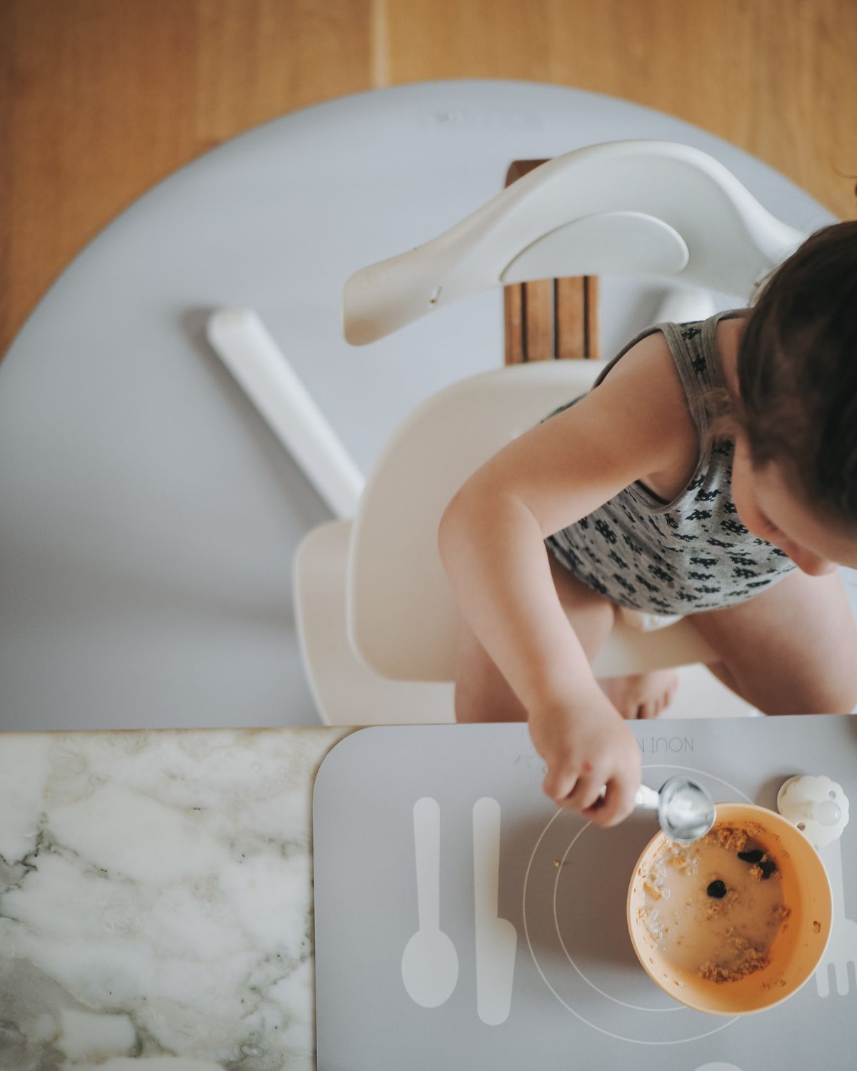 A grey powder learning placemat with illustrations of a plate, fork, knife, and spoon on it. Paired with a round grey powder floor mat under a child high chair.