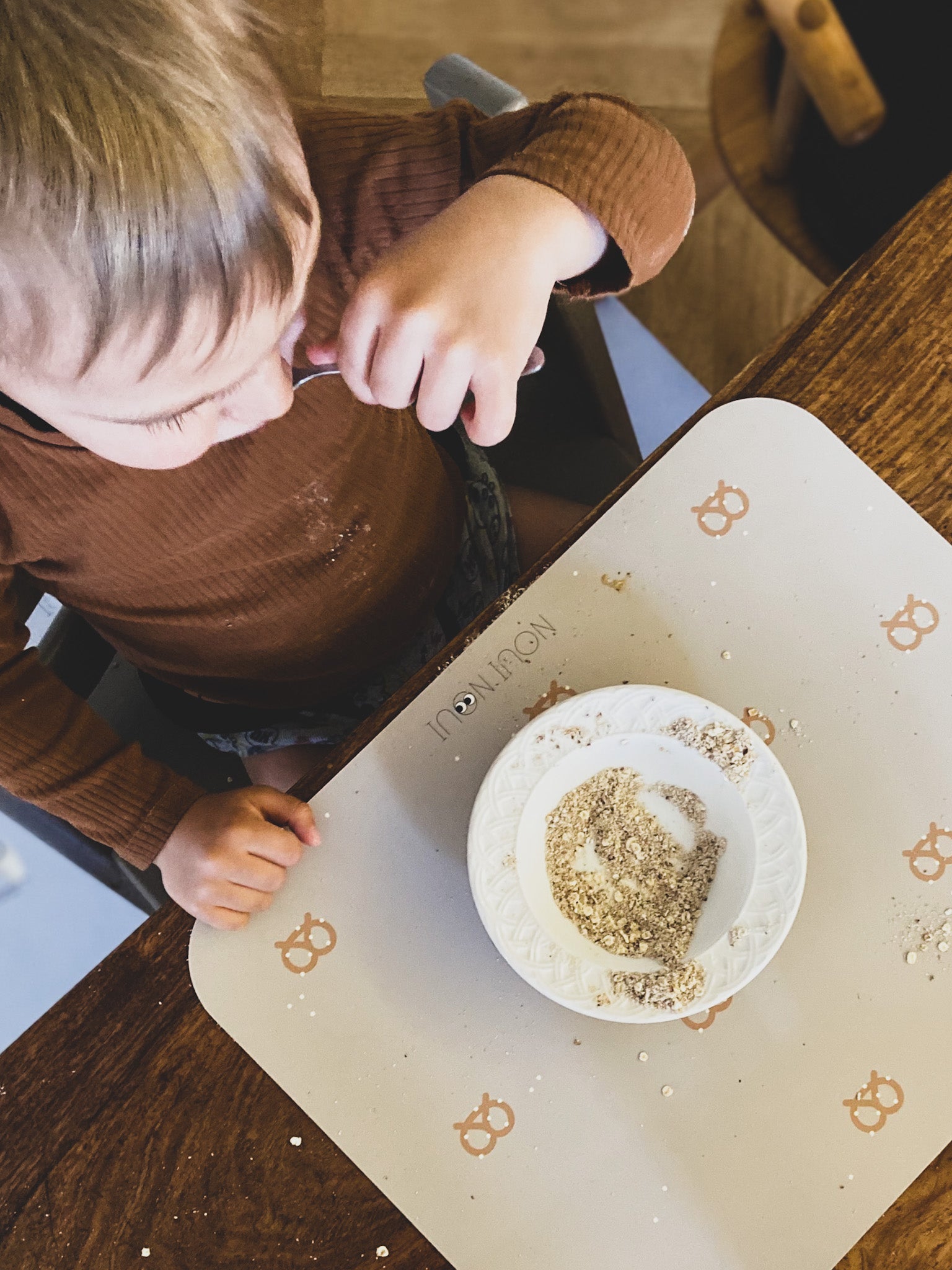 Child eating cereal on our Placemat in nude tone with a pattern of pretzels and salt.