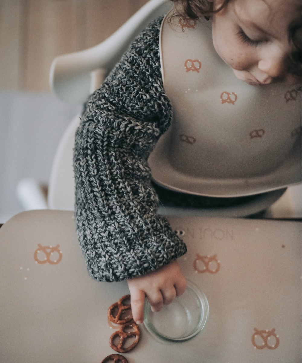 Placemat in nude tone with a pattern of pretzels and salt wearing our nude silicone bib with pretzels.