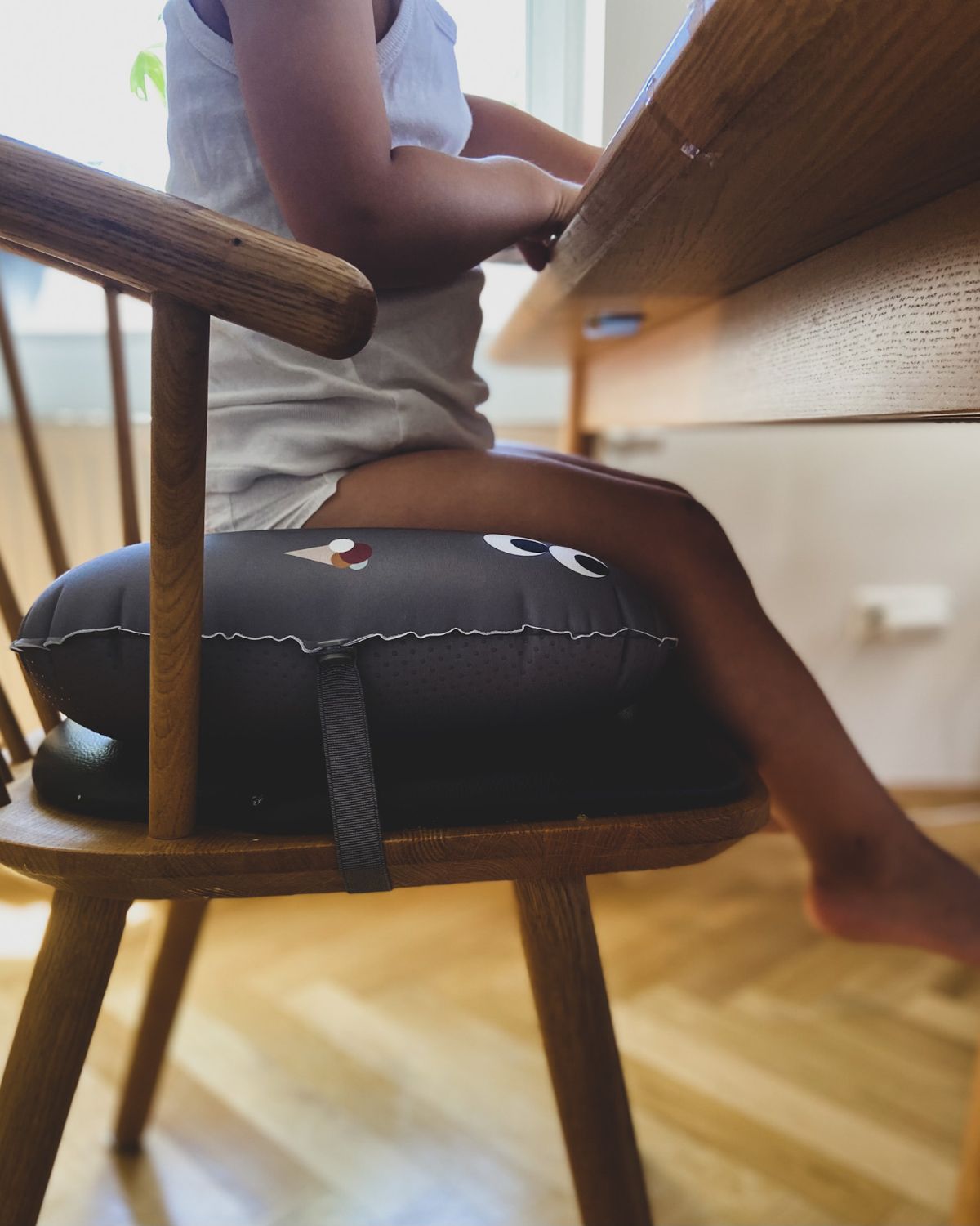 alt="Inflatable ergonomic booster cushion for children with elastic strap and anti-slip backing, placed on a dining chair"