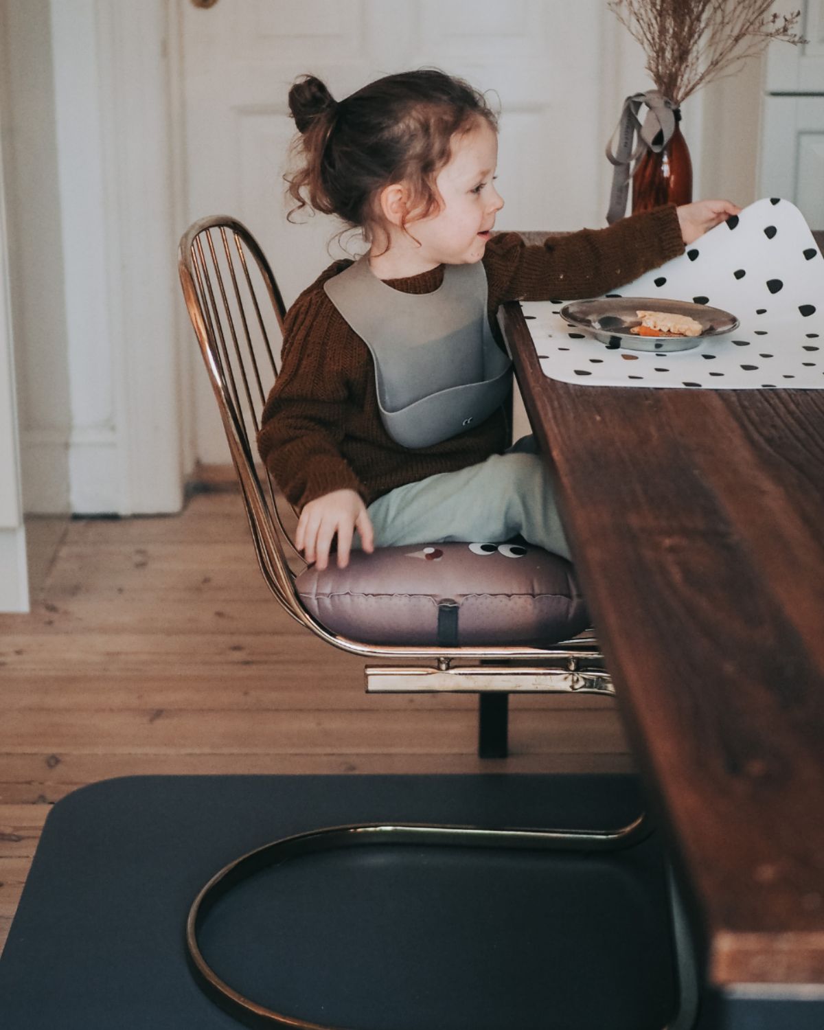 alt="Inflatable ergonomic booster cushion for children with elastic strap and anti-slip backing, placed on a dining chair"