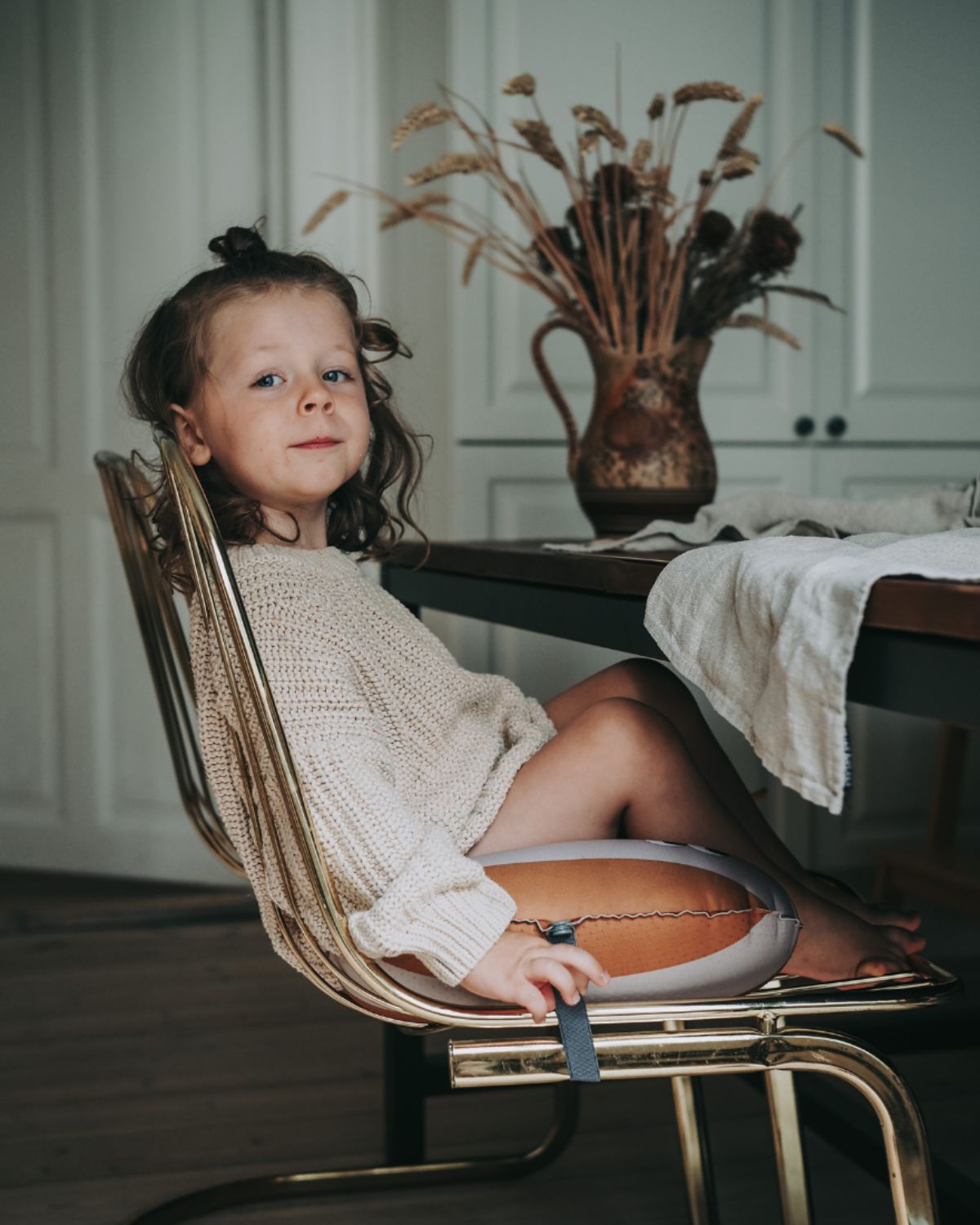 alt="Inflatable ergonomic booster cushion for children with elastic strap and anti-slip backing, placed on a dining chair"