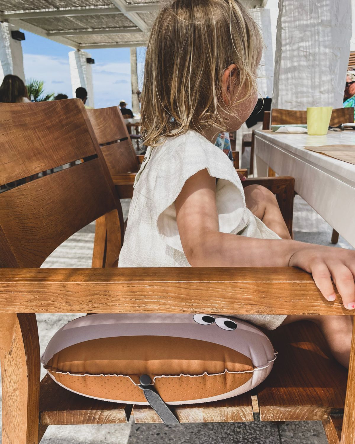 alt="Inflatable ergonomic booster cushion for children with elastic strap and anti-slip backing, placed on a dining chair"