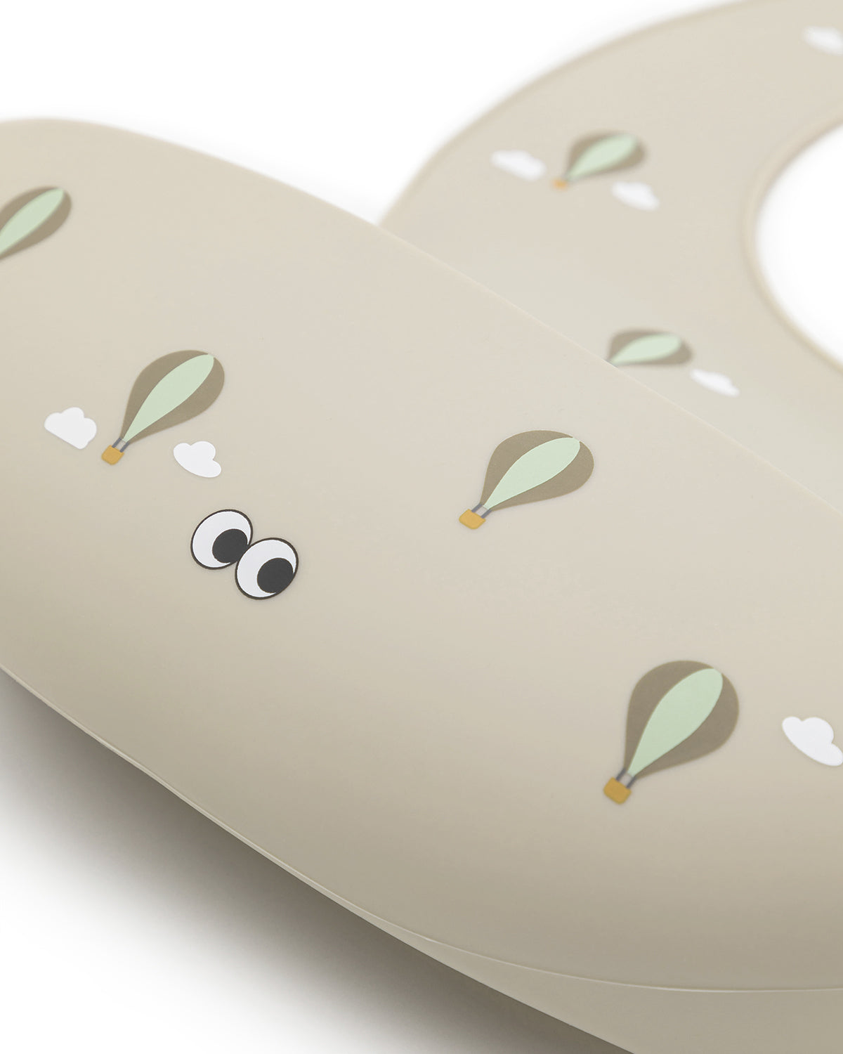 A closeup of our nude silicone bib with small cute hot air balloon pattern and an adjustable neck strap.