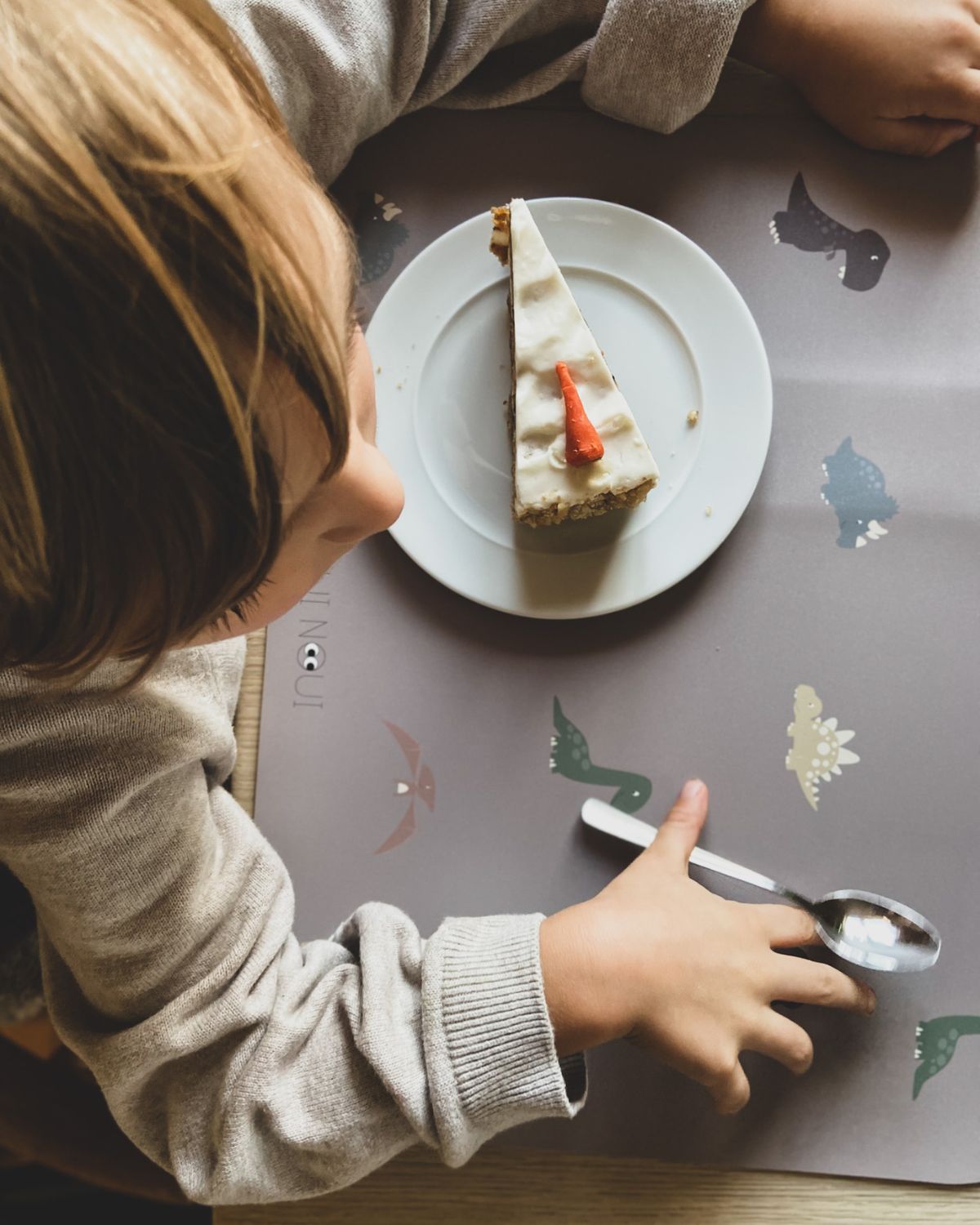 A child eating cake on our Placemat with various illustrations of dinosaurs in shades of green, brown, and gray, on a cocoa background.