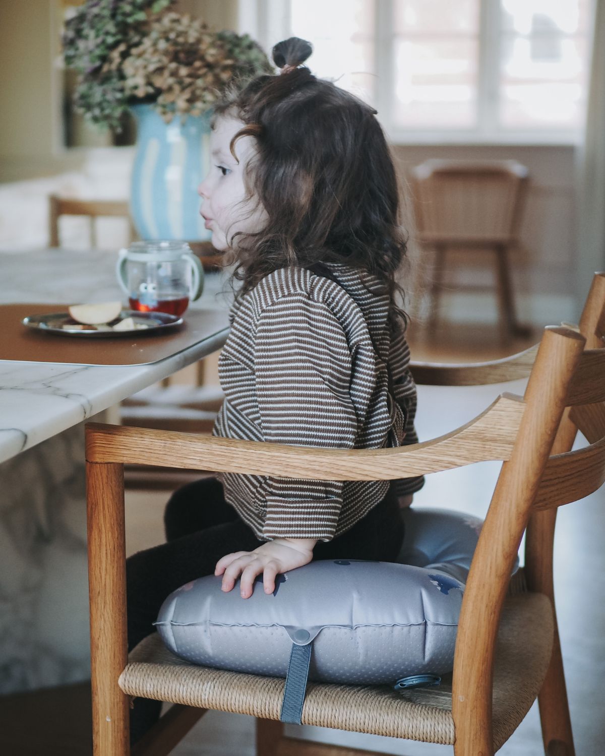 alt="Inflatable ergonomic booster cushion for children with elastic strap and anti-slip backing, placed on a dining chair"