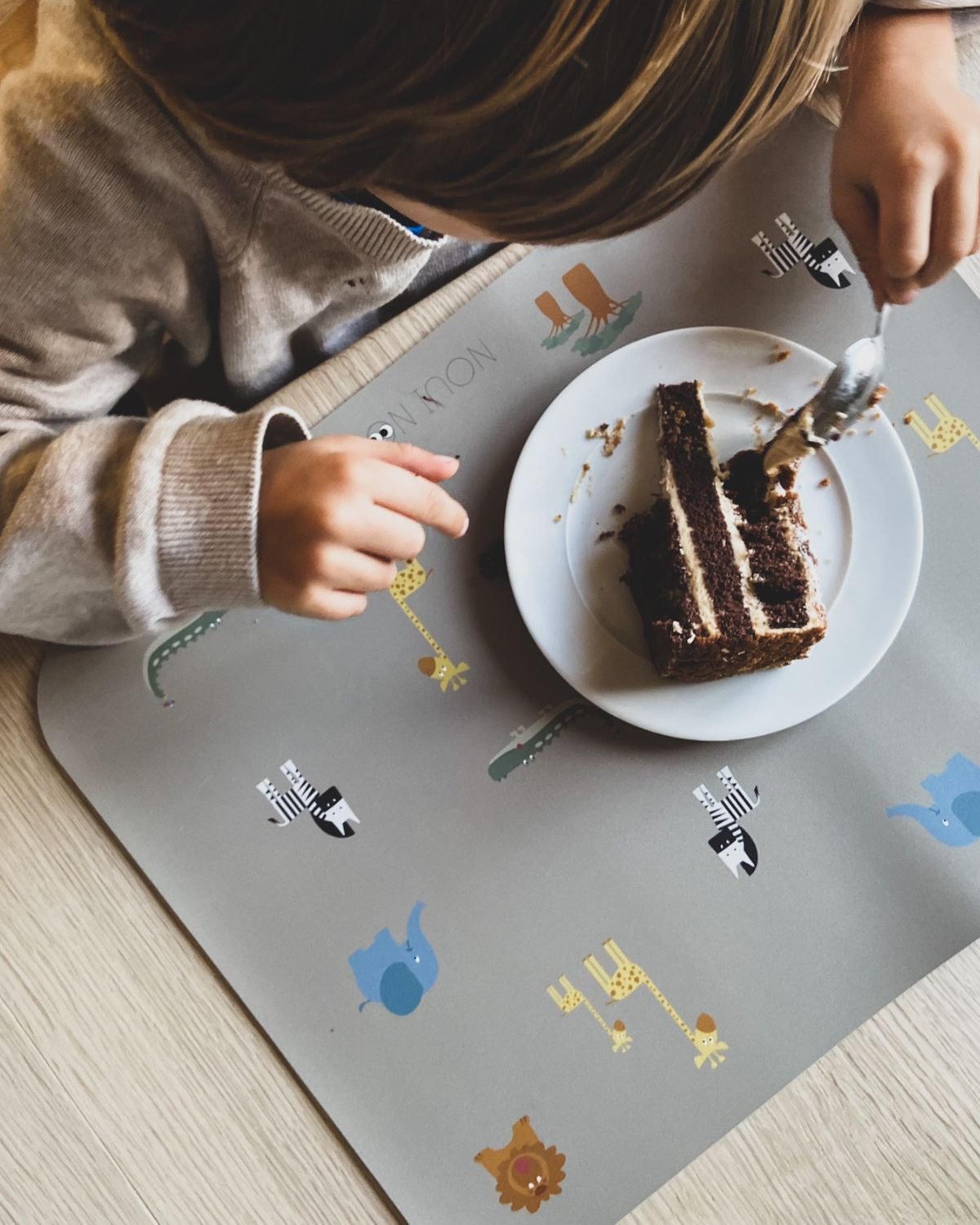 A child eating cake on our Placemat with various cute safari animals including an elephant, giraffe, and other safari animals.