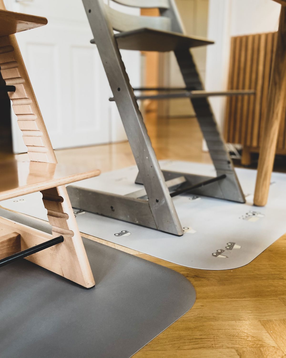 A rectangular grey powder high chair floor mat with a pattern of little wheels and vehicles in stylish grey tones.
