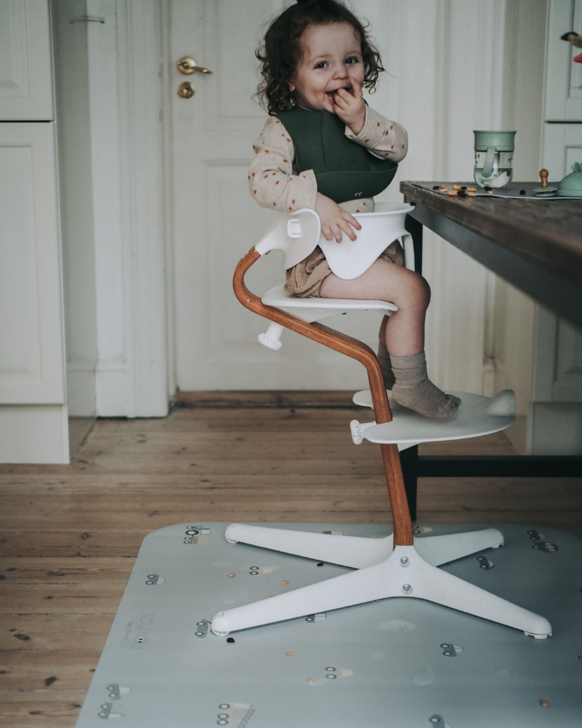 A rectangular grey powder high chair floor mat with a pattern of little wheels and vehicles in stylish grey tones.