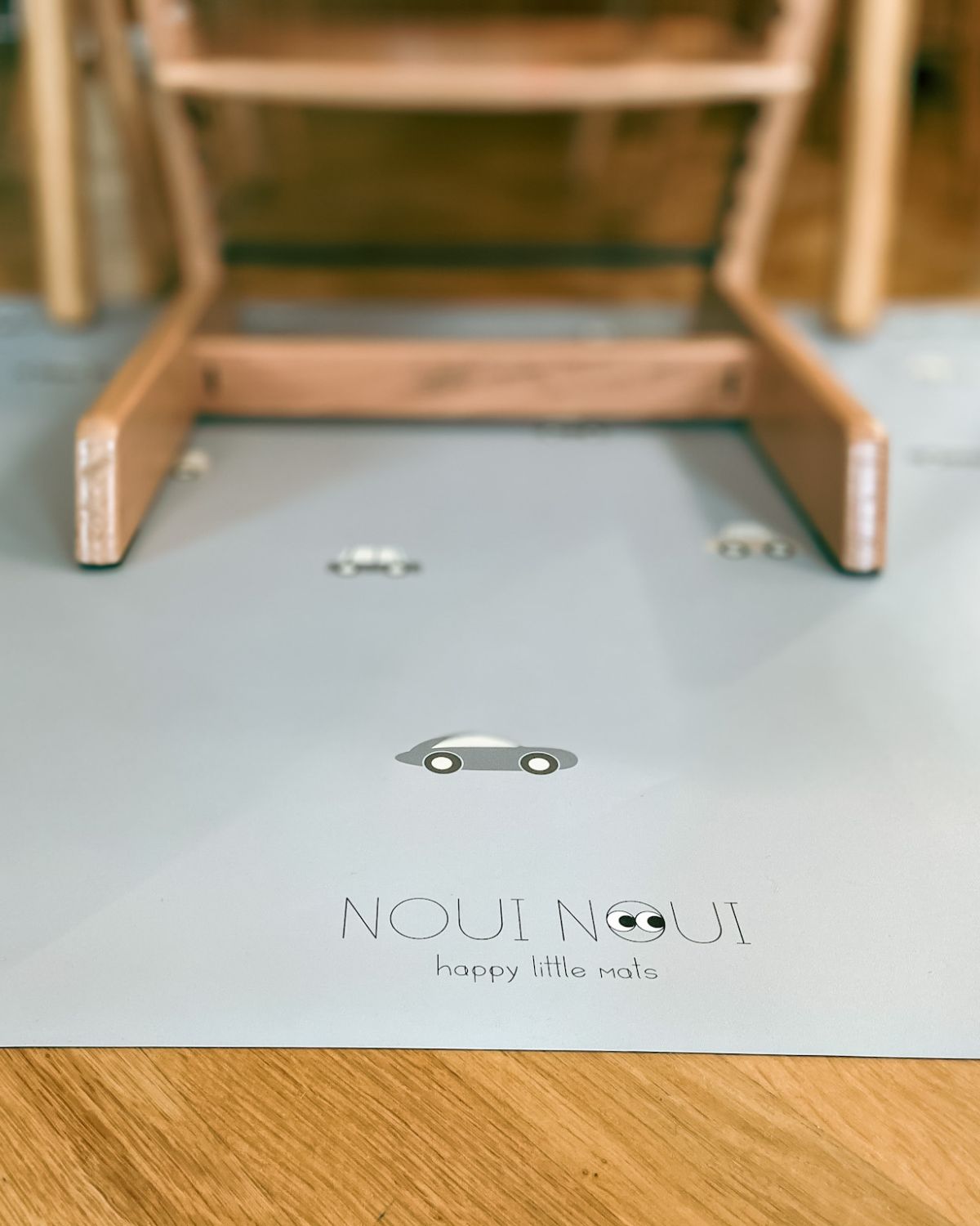 A rectangular grey powder high chair floor mat with a pattern of little wheels and vehicles in stylish grey tones.