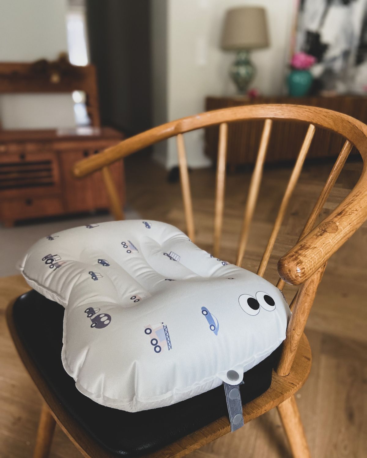 alt="Inflatable ergonomic booster cushion for children with elastic strap and anti-slip backing, placed on a dining chair"