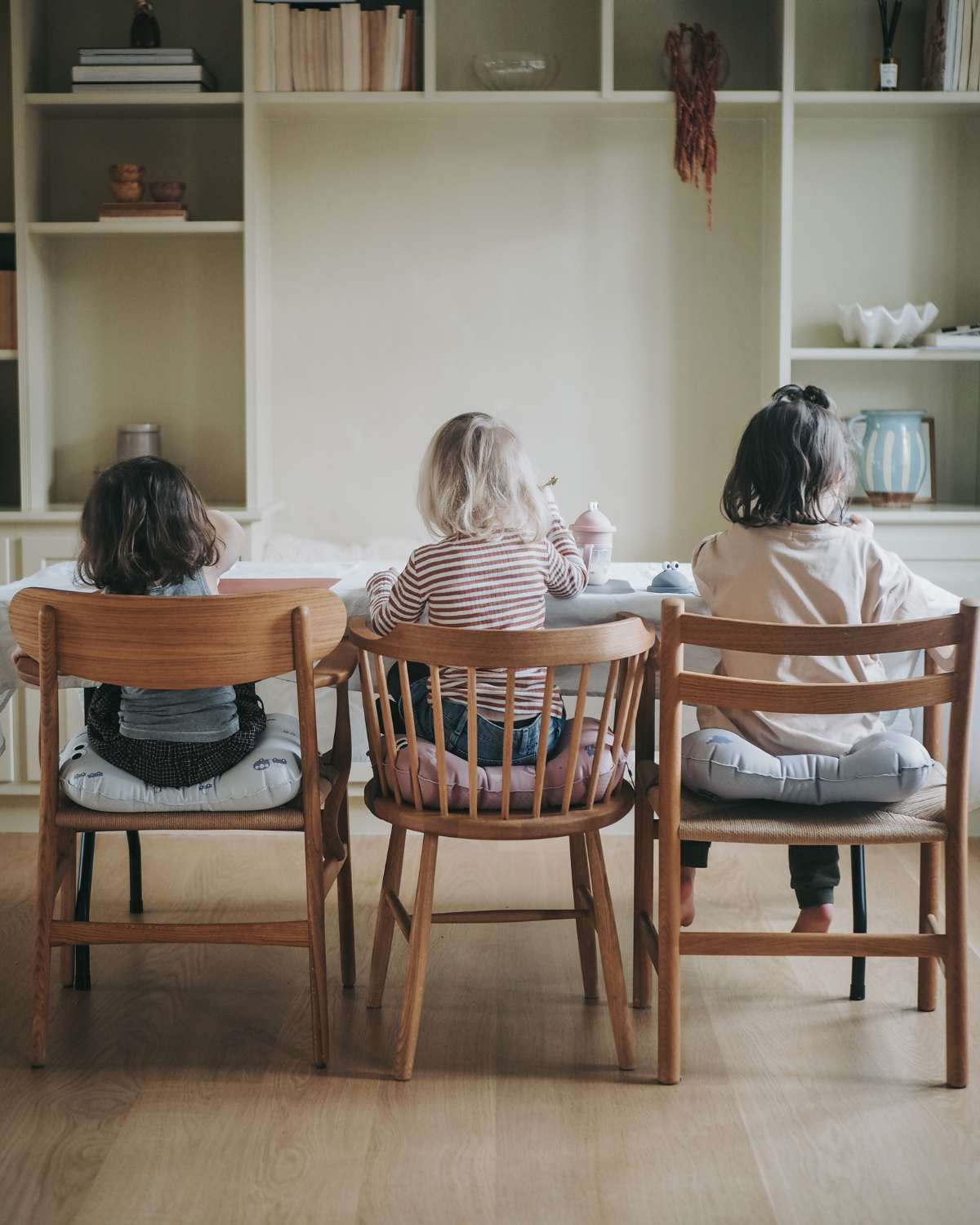alt="Inflatable ergonomic booster cushion for children with elastic strap and anti-slip backing, placed on a dining chair"