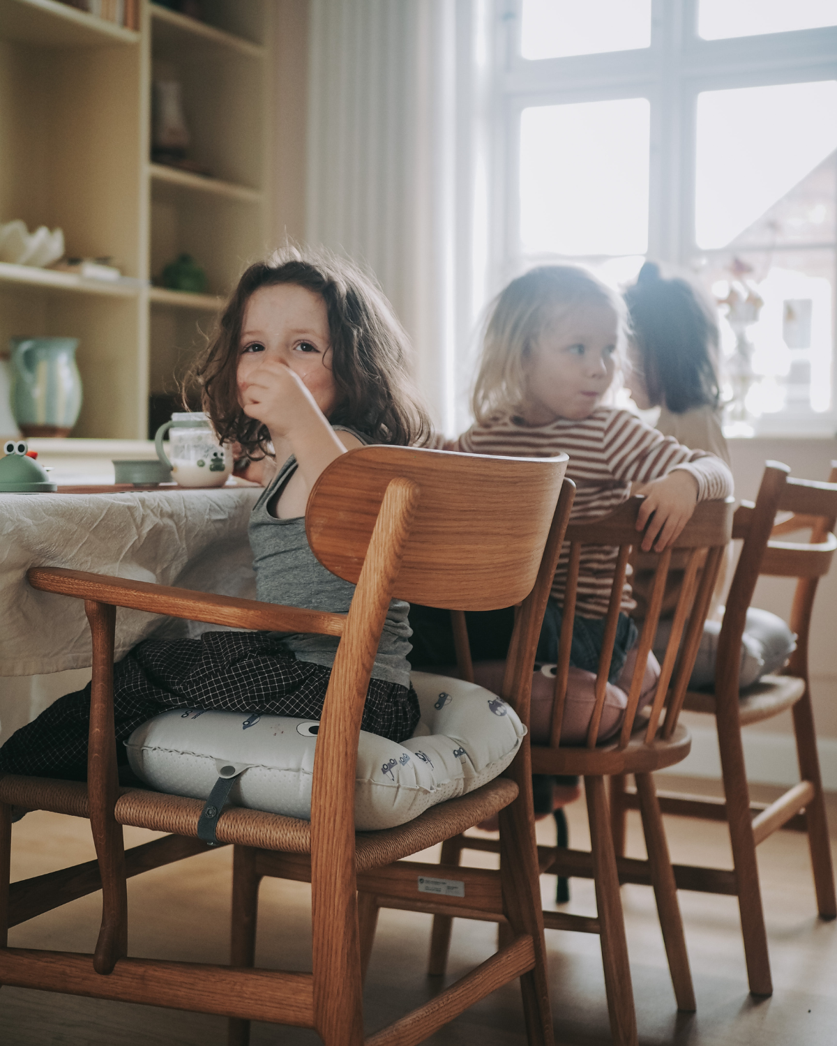 alt="Inflatable ergonomic booster cushion for children with elastic strap and anti-slip backing, placed on a dining chair"