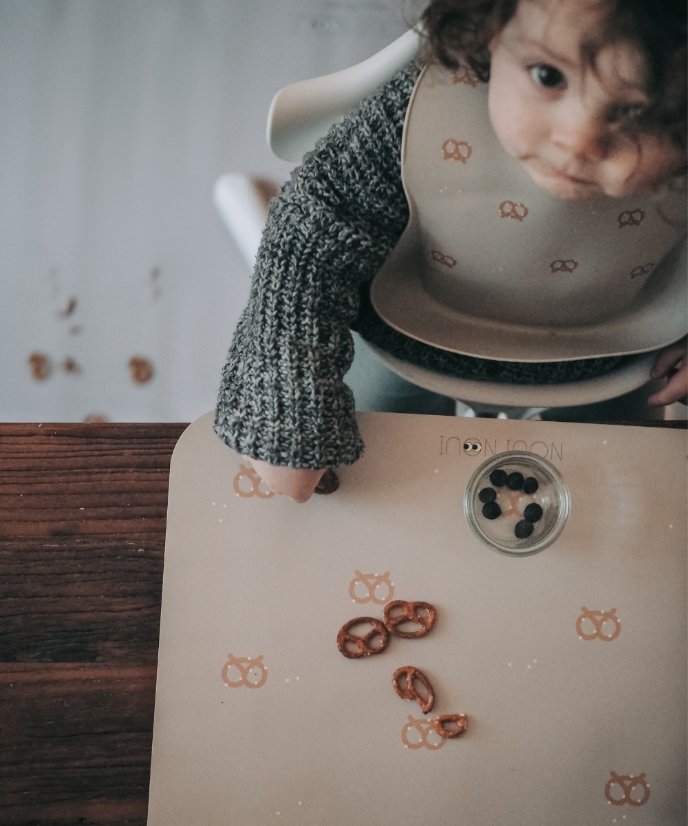 Child eating pretzels on our Placemat in nude tone with a pattern of pretzels and salt.
