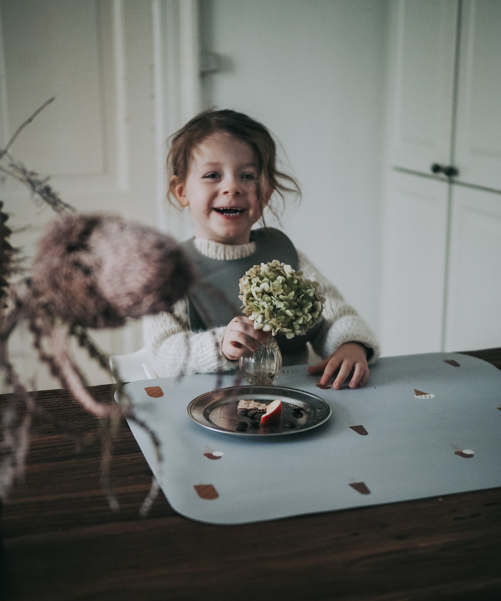 A child sitting with a flower on our grey placemat with a pattern of various ice cream designs across the surface.