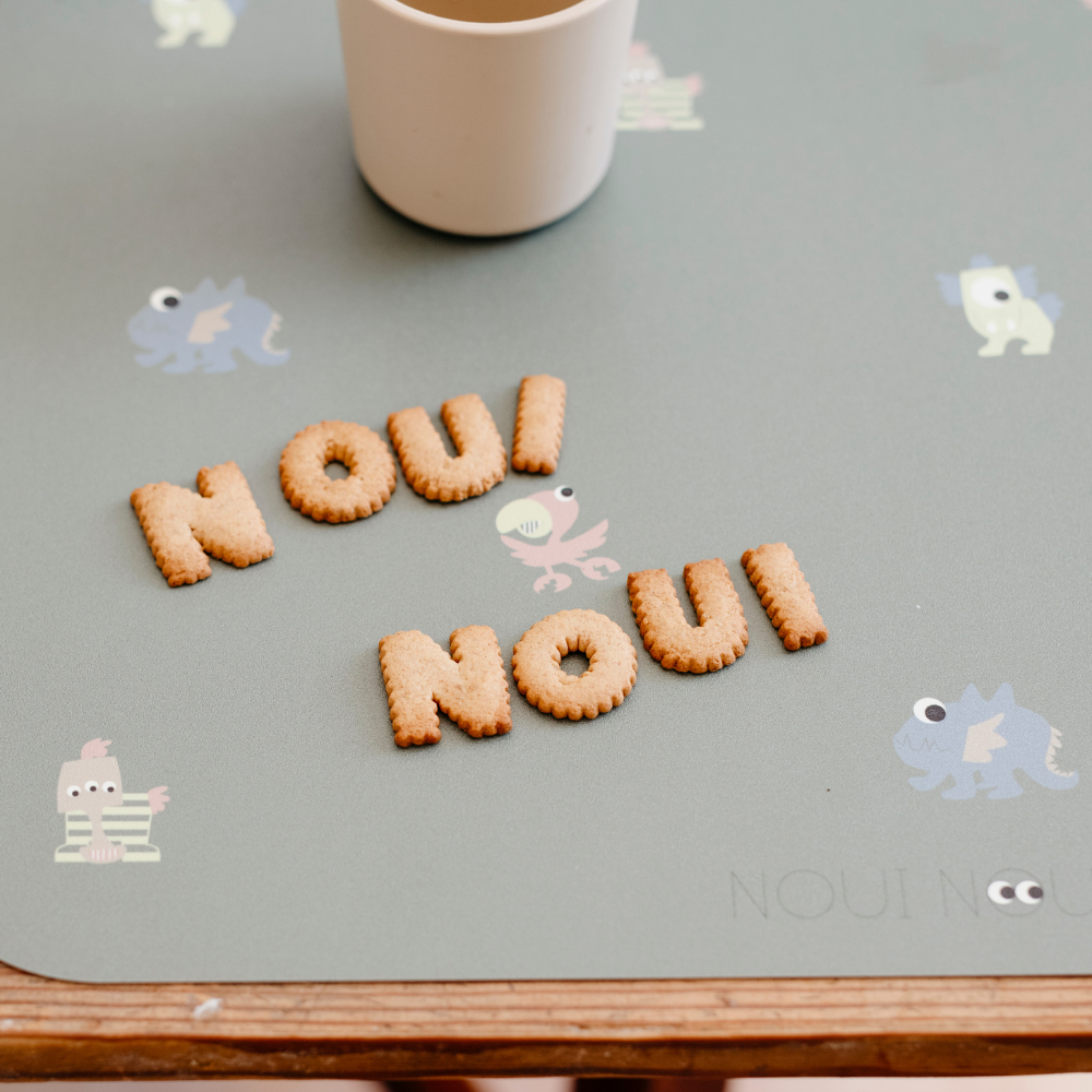 Alphabet cookies on our Placemat with dusty olive background featuring a playful pattern of various small, friendly fantasy animal fable icons.