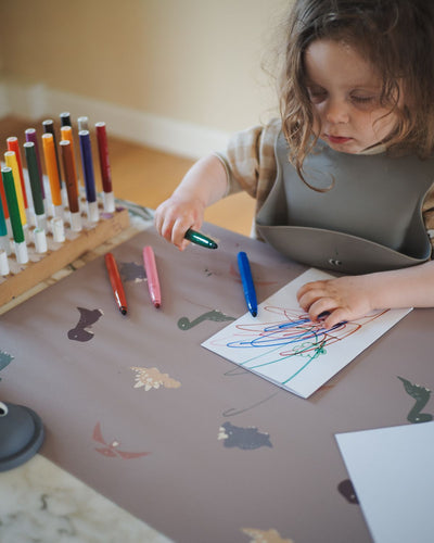 A XL placemat with cute dinosaur pattern on a cocoa background. Perfect for arts and crafts and protection of the table surface.