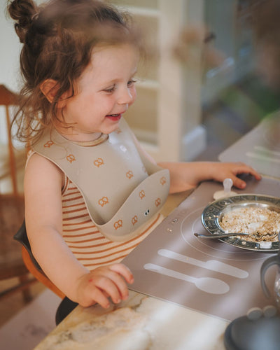 A cocoa brown learning placemat with illustrations of a plate, fork, knife, and spoon on it. Perfect helper when the child wants to help setting the table.