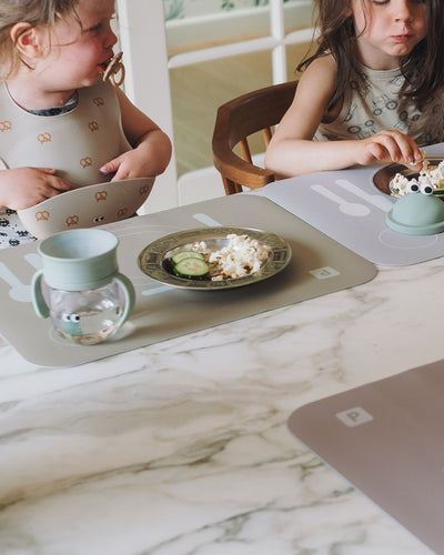 A learning placemat in olive haze gray with illustrations of a plate, fork, knife, and spoon on it. Perfect helper when the child wants to help setting the table. Mixed with grey and cocoa placemat.
