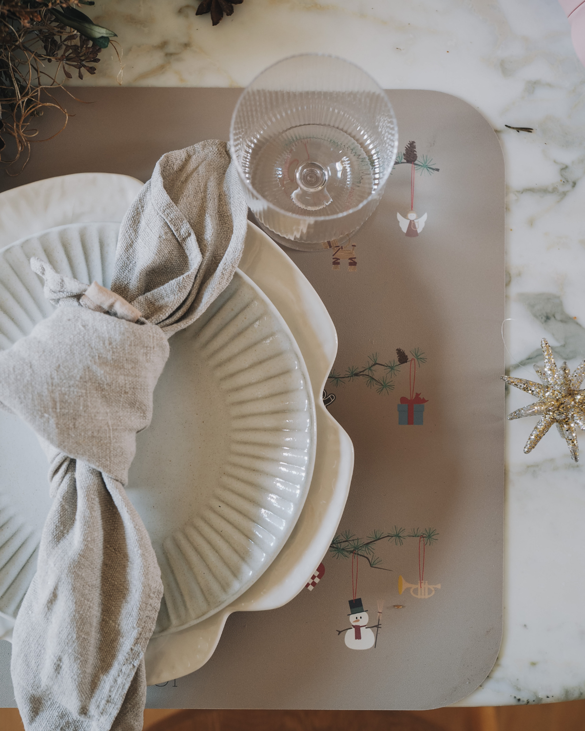 Plate on our olive haze gray placemat with Christmas-themed decorations including snowmen, hearts, angel on fir branch.