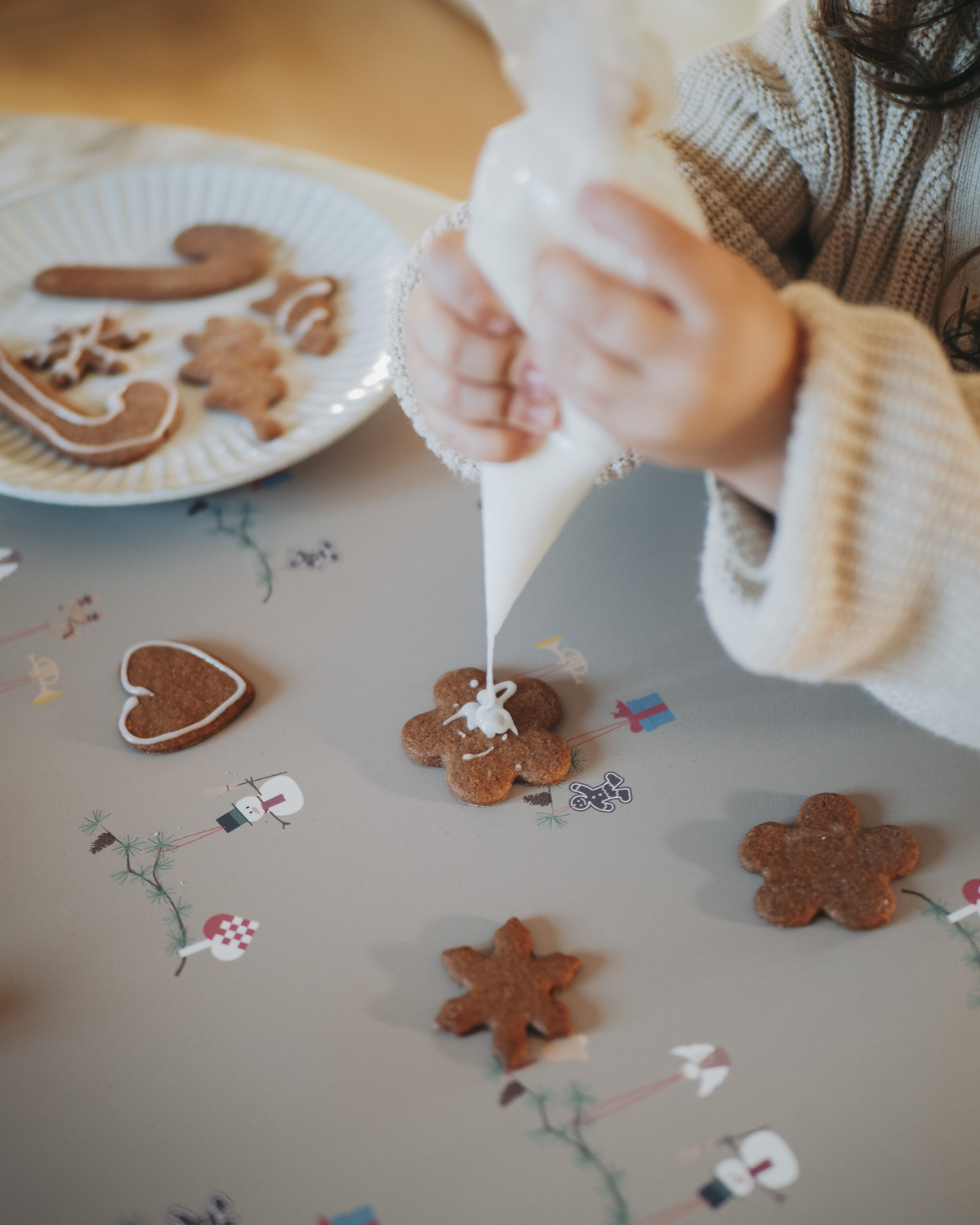 A child decorating cookies on our olive haze gray placemat with Christmas-themed decorations including snowmen, hearts, angel on fir branch.