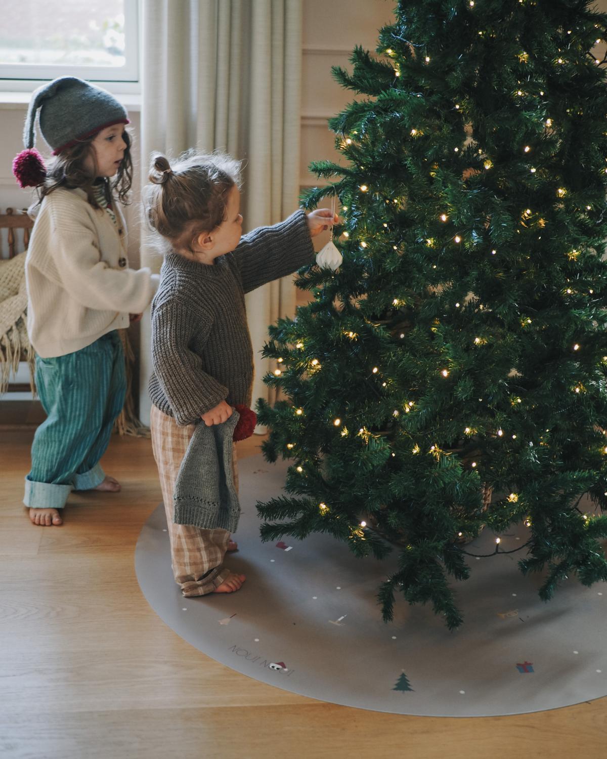 Children looking a Christmas tree which is on our round vinyl floor mat with a Christmas theme, featuring holiday icons such as snowflakes, a Christmas tree, and angel.