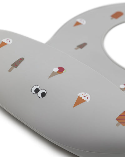 Closeup of our silicone bib with cute ice creams on a grey powder background. Extra large cup and a adjustable strap in the neck.