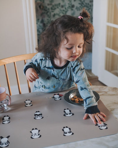 Placemat with a nude background and multiple illustrations of pandas in various moods, such as happiness, sadness and many other moods.