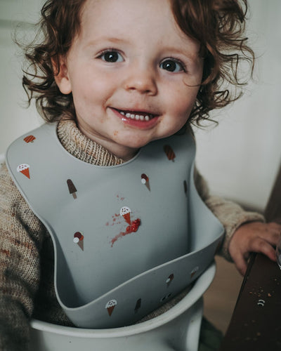A child wearing our silicone bib with cute ice creams on a grey powder background. Extra large cup and a adjustable strap in the neck.