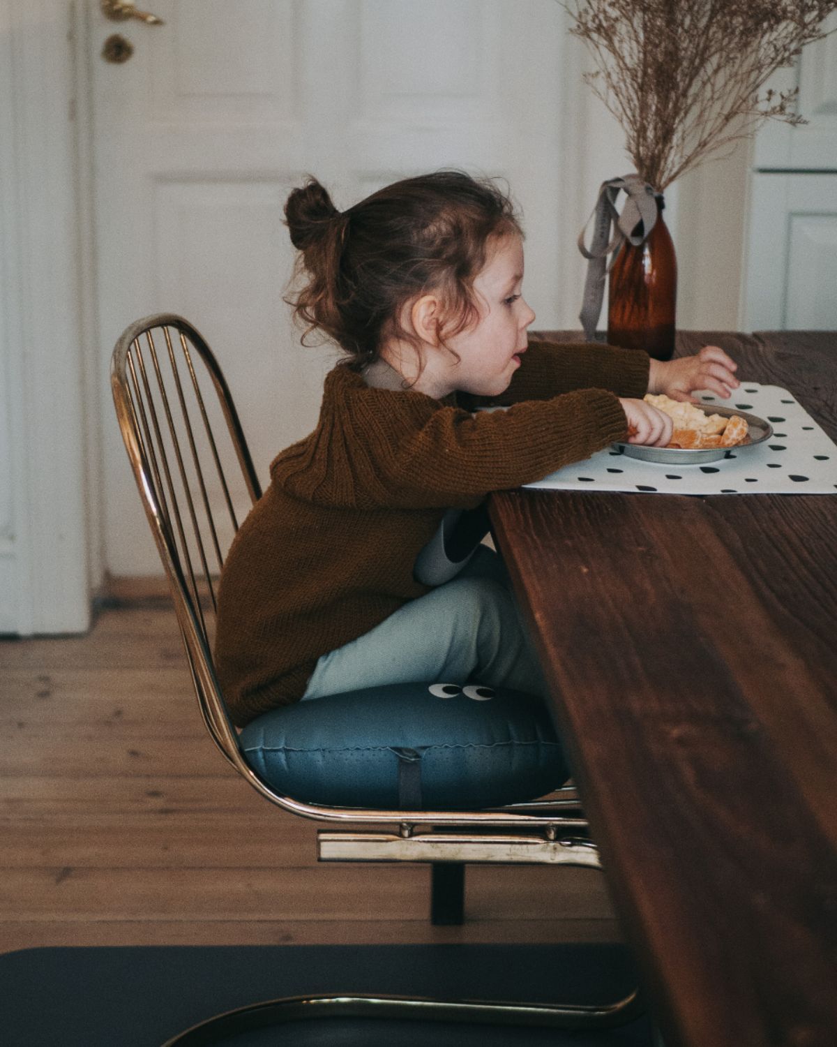 alt="Inflatable ergonomic booster cushion for children with elastic strap and anti-slip backing, placed on a dining chair"