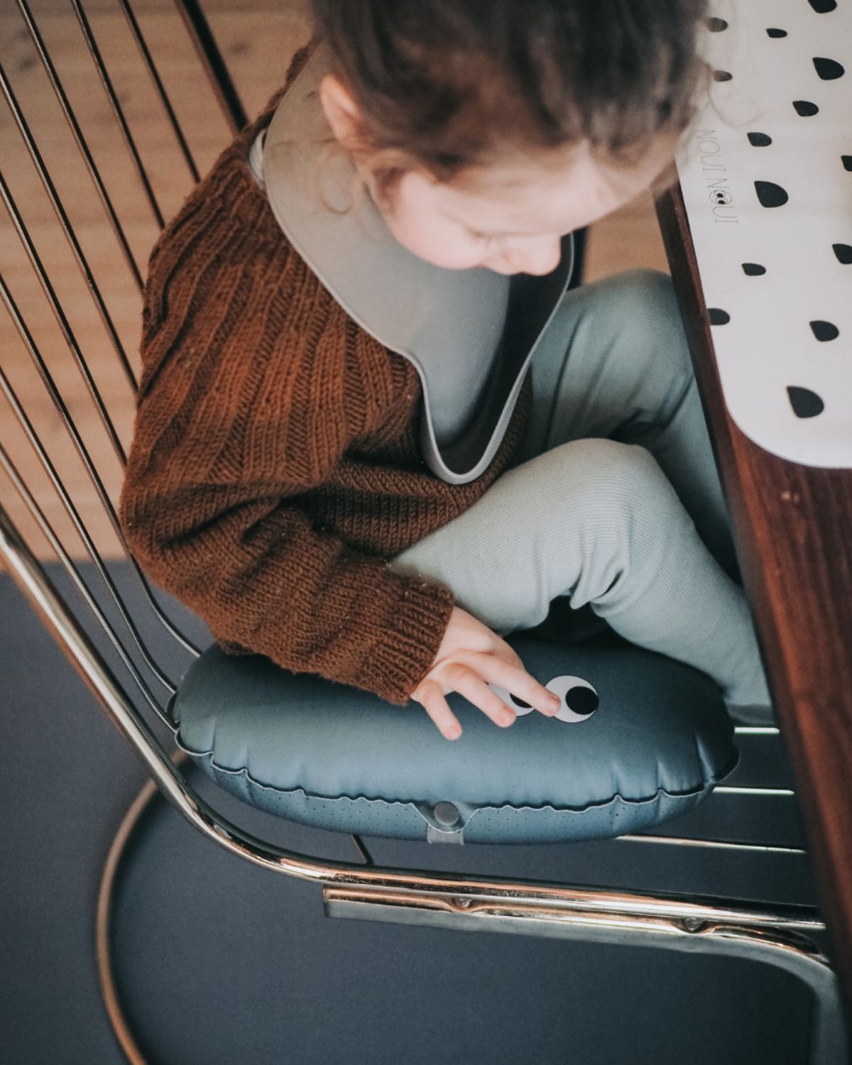 alt="Inflatable ergonomic booster cushion for children with elastic strap and anti-slip backing, placed on a dining chair"