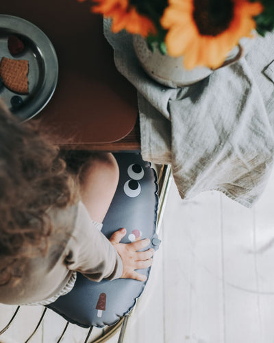alt="Inflatable ergonomic booster cushion for children with elastic strap and anti-slip backing, placed on a dining chair"