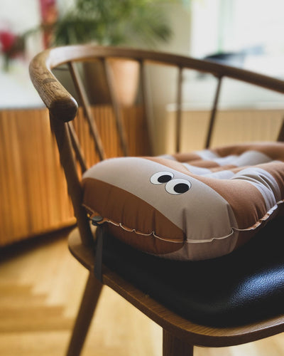 alt="Inflatable ergonomic booster cushion for children with elastic strap and anti-slip backing, placed on a dining chair"