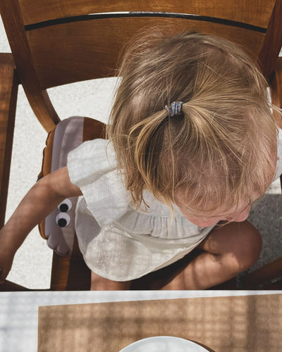 alt="Inflatable ergonomic booster cushion for children with elastic strap and anti-slip backing, placed on a dining chair"