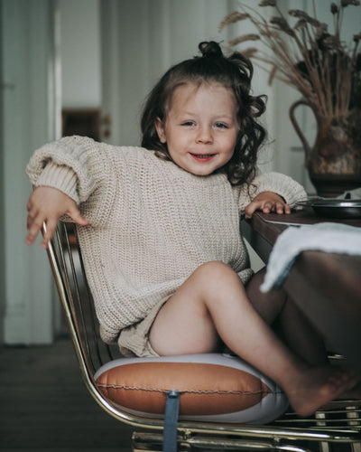 alt="Inflatable ergonomic booster cushion for children with elastic strap and anti-slip backing, placed on a dining chair"