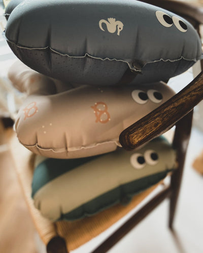 alt="Inflatable ergonomic booster cushion for children with elastic strap and anti-slip backing, placed on a dining chair"