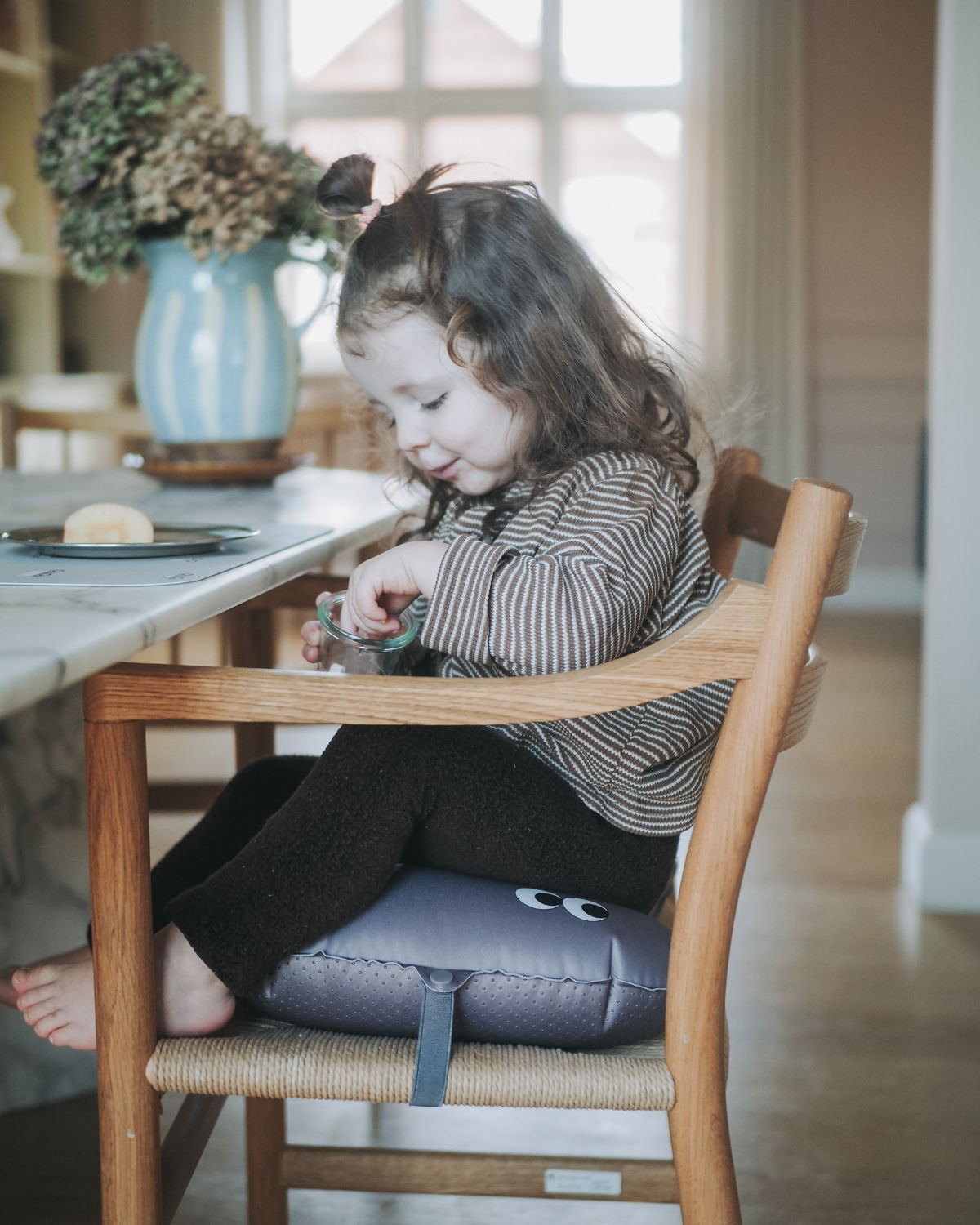 alt="Inflatable ergonomic booster cushion for children with elastic strap and anti-slip backing, placed on a dining chair"