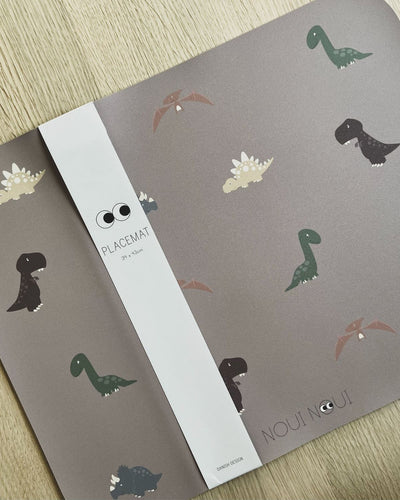 Placemat with various illustrations of dinosaurs in shades of green, brown, and gray, on a cocoa background.
