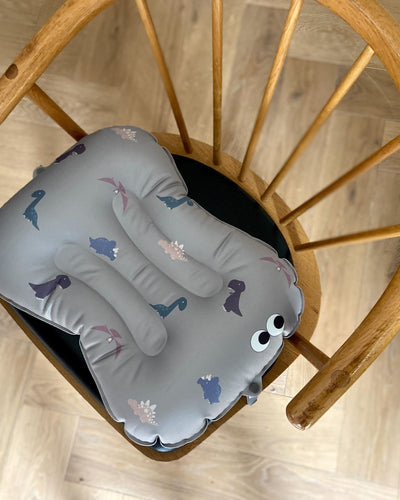 alt="Inflatable ergonomic booster cushion for children with elastic strap and anti-slip backing, placed on a dining chair"