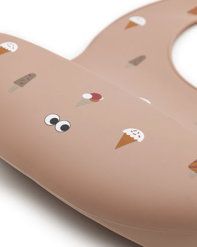 A closeup of our silicone bib in dusty rose color with a pattern of different cute ice cream. The bib has an adjustable strap and an extra large cup to catch food and fluids. 