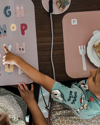 A rose-colored learning placemat with illustrations of a plate, fork, knife, and spoon, and sections marked for 'cutlery,' 'plates,' and 'drinks.' Paired with our ABC XL placemat.