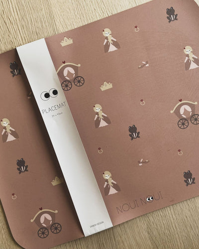 A placemat with a princess-themed pattern including illustrations of princesses, castles, and hearts in pink tones.