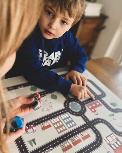 An XL placemat with different small cars and road map design, featuring buildings, trees, and a Ferris wheel.