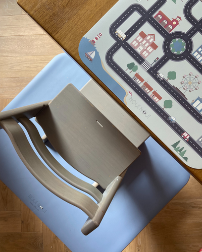 An XL placemat with different small cars and road map design, featuring buildings, trees, and a Ferris wheel. Paired with a dusty blue floor mat. 