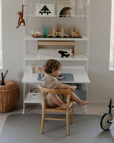 A high chair floor mat made of soft vinyl, in the color olive haze gray. A rectangular mat to protect all kind of floors from spills. Put it under the high chair. Easy to clean.