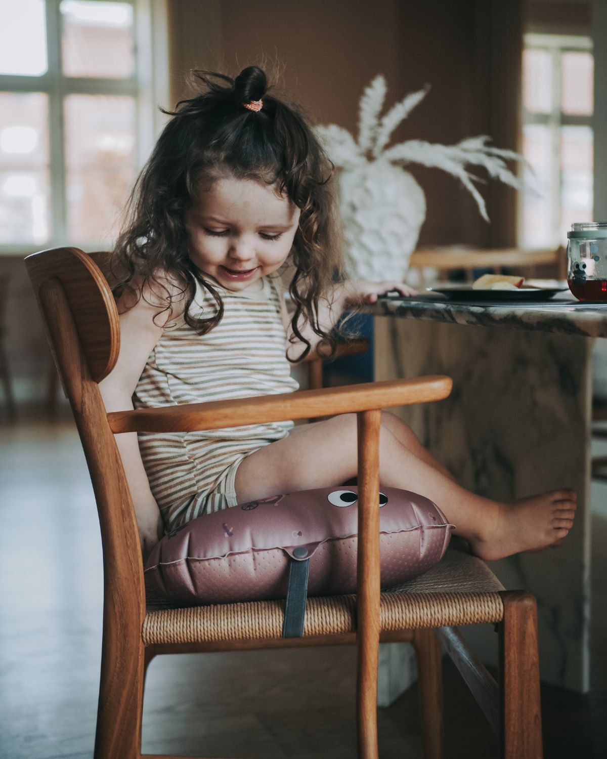 alt="Inflatable ergonomic booster cushion for children with elastic strap and anti-slip backing, placed on a dining chair"