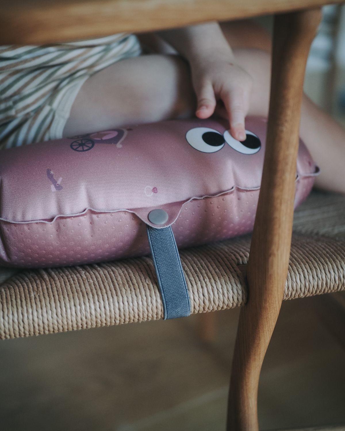 alt="Inflatable ergonomic booster cushion for children with elastic strap and anti-slip backing, placed on a dining chair"