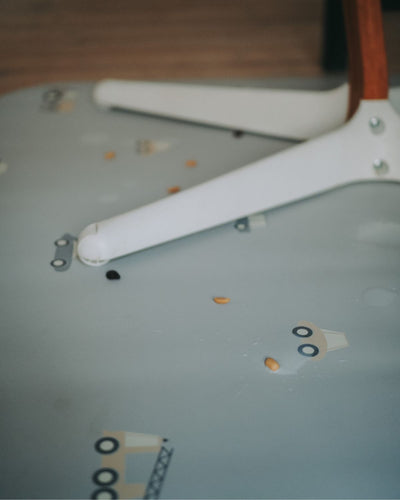 A rectangular grey powder high chair floor mat with a pattern of little wheels and vehicles in stylish grey tones.