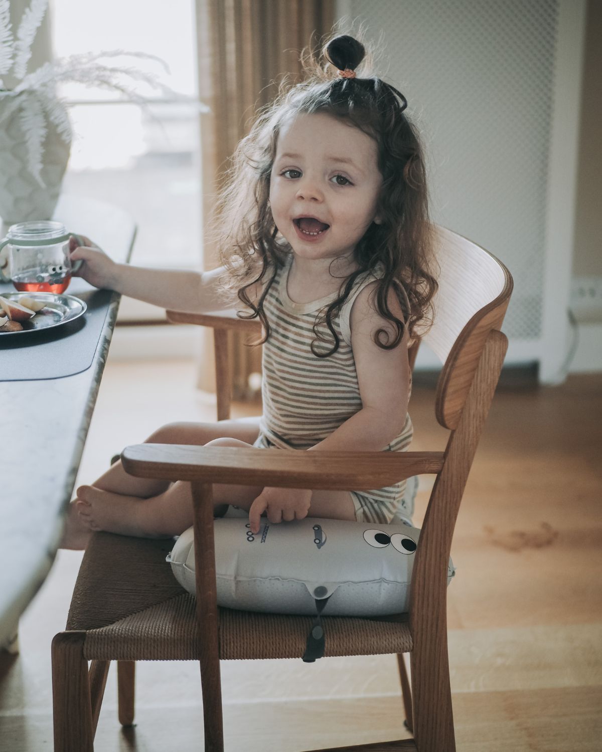 alt="Inflatable ergonomic booster cushion for children with elastic strap and anti-slip backing, placed on a dining chair"